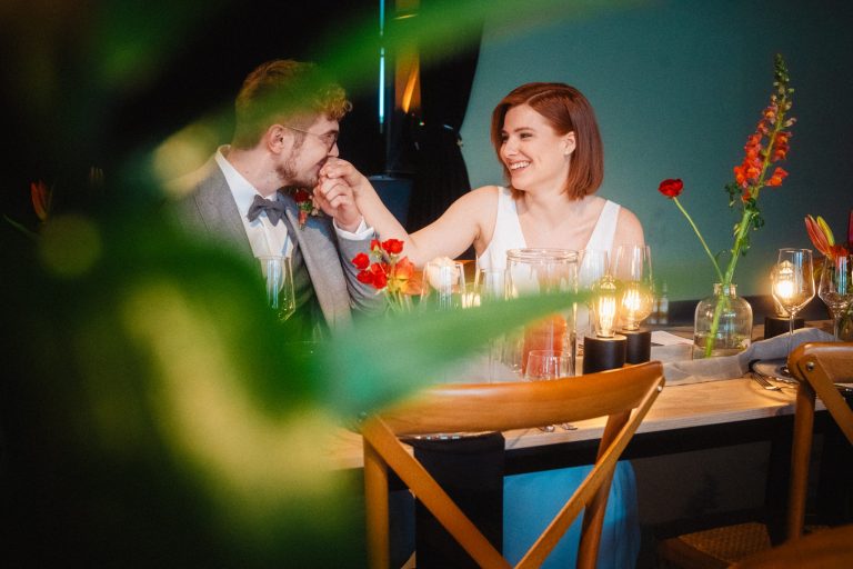 Brautpaar am Tisch, er küsst ihre Hand