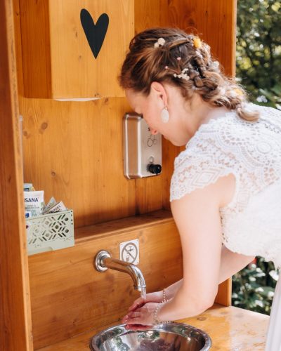 Braut wäscht sich am Waschbecken von Kompotoi die Hände