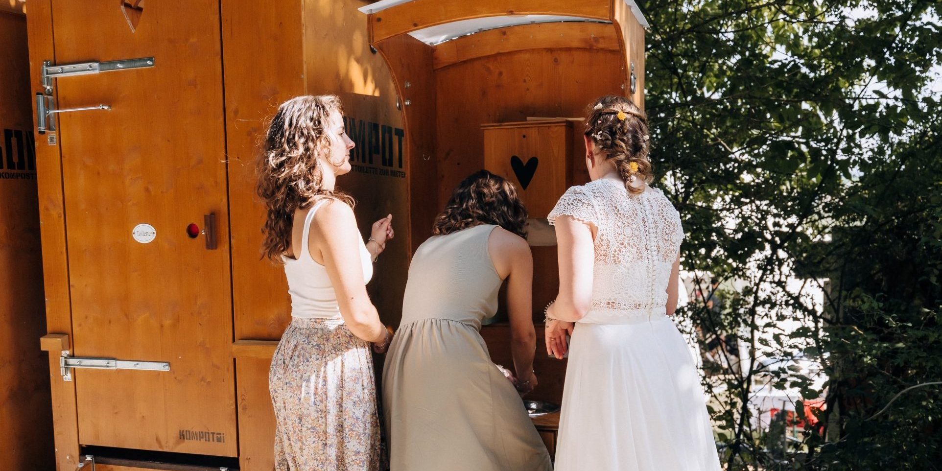 Kompotoi mit Waschbecker an dem gerade braut und Freundinnen sich die Hände waschen